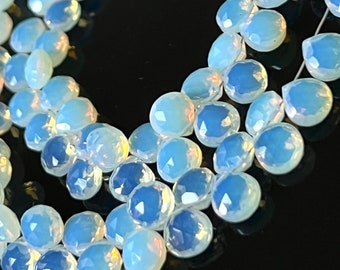 May include: A strand of iridescent blue opal gemstone beads, faceted and strung on a wire. The beads are teardrop shaped and have a translucent, milky quality.