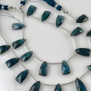 May include: A strand of dark blue gemstone beads with a faceted, teardrop shape. The beads are strung on a silver wire and have a subtle sparkle.