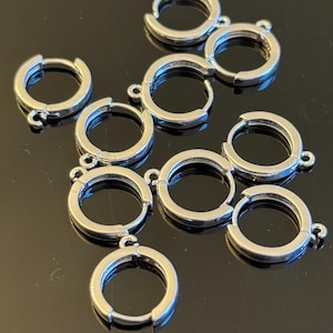May include: Ten silver-toned earring hoops with a jump ring attached to each hoop. The hoops are all the same size and are arranged in a random pattern.