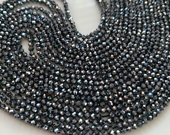 May include: A strand of black faceted gemstone beads. The beads are small and round, with a shiny, metallic finish.
