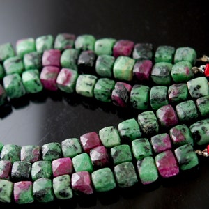 May include: A strand of green and pink gemstone beads, with a square shape, strung on a cord with red tassels at the ends.