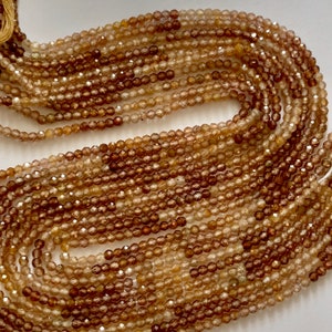 May include: A strand of brown and gold gemstone beads. The beads are faceted and have a round shape. The beads are strung on a clear thread.