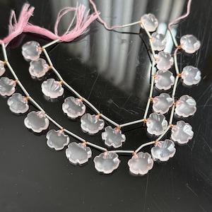 May include: Strands of pale pink flower-shaped beads. The beads are strung on thin, silver-colored wire with pink thread at the ends. The beads have a translucent quality and are arranged in multiple rows.