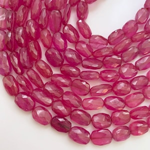 May include: Close-up of a strand of faceted, oval-shaped ruby beads. The beads are a deep, rich red color with a polished, reflective surface. The gemstones are strung together, creating a necklace or bracelet.