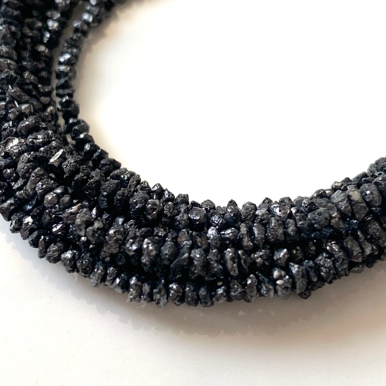May include: A strand of black diamond beads. The beads are rough and irregular in shape, giving the strand a rustic look.
