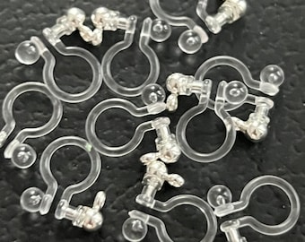 May include: A group of clear plastic earring backs with silver metal posts and balls. The backs are designed to hold earrings in place.