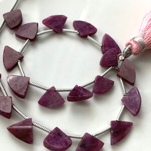 May include: A strand of purple gemstone beads, each bead is a half-circle shape, strung on a silver wire with a pink tassel at the end.