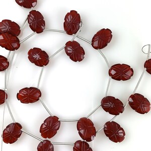 May include: A strand of dark red carnelian beads with a carved design. The beads are oval shaped and strung on a silver wire.