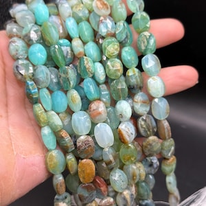 May include: Strands of faceted gemstone beads in shades of teal, green, and brown. The beads are oval-shaped and strung together, with a tassel at the end. The gemstones have a polished, glossy finish. The beads are approximately 0.5 inches in length.