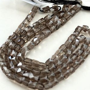 May include: Strands of faceted, smoky quartz beads. The beads are a translucent, brownish-gray color and are strung together. The facets catch the light, creating a sparkling effect. The beads are likely for jewelry making.