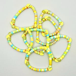 May include: A set of five colorful bracelets with yellow rubber duck charms. The bracelets are made of layered, colorful, round beads.