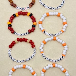May include: Eight colorful beaded bracelets with different phrases, including "Andor", "Cassian Andor", "B2EMO", "Kino Loy", "Fight the Empire", "On Program", "Theres Only", and "One Way Out".