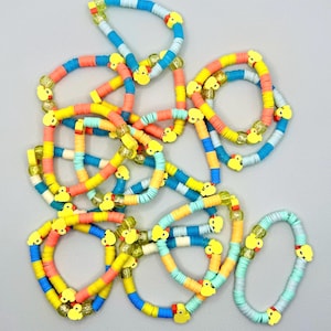May include: A pile of colorful bracelets with yellow rubber ducky charms. The bracelets are made of layered plastic beads in shades of blue, yellow, orange, and pink.