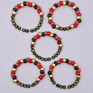 May include: Five beaded bracelets with red, black, and gold beads. The bracelets have text that reads "TOWER OF TERROR", "HTH", "TWILIGHT ZONE", "DROP IN", and "IF YOU DARE" in yellow letters.