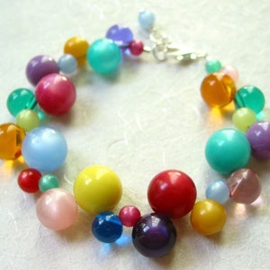 May include: A colorful beaded bracelet with a variety of round beads in shades of blue, green, yellow, red, orange, and purple. The bracelet is made with a silver clasp.