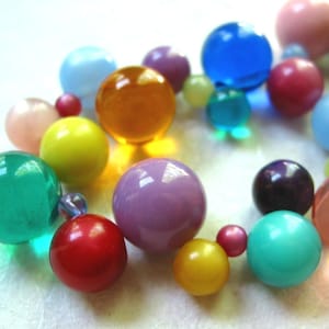 May include: A colorful assortment of round glass beads in various colors, including pink, blue, green, yellow, orange, and purple. The beads are arranged in a circle, creating a decorative and eye-catching display.