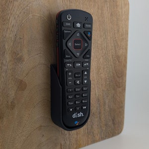 May include: A black remote control with a red accent and the word "dish." printed on the bottom. The remote has buttons for DVR, Guide, Options, Select, Back, Live TV, Info, and more. The remote is mounted on a wooden wall.