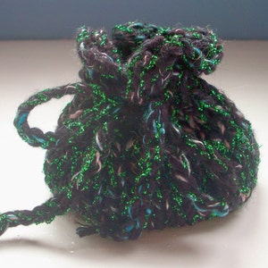 May include: A small black and green drawstring bag made of yarn with glitter. The bag is tied at the top and has a long, loose drawstring.