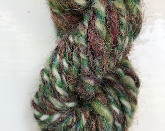 May include: A skein of yarn in a mix of green, brown, white, and blue colors. The yarn is soft and fluffy, and it has a rustic look.