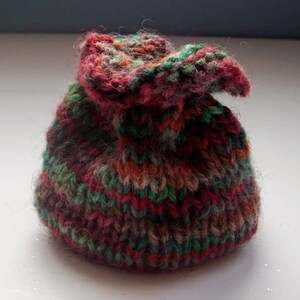May include: A small, hand-knitted pouch with a drawstring closure. The pouch is made with a multi-colored yarn in shades of red, green, brown, and orange.