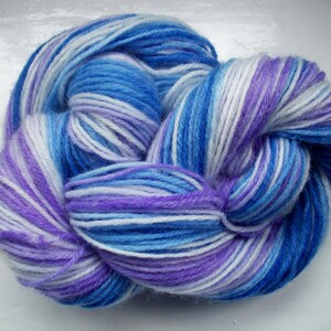 May include: A skein of colorful yarn in shades of blue, purple, and white. The yarn is tightly wound, showing a mix of light and dark hues. The yarn is suitable for knitting or crocheting projects.