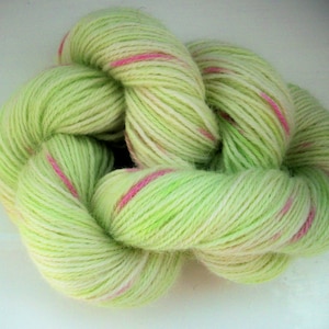May include: A skein of yarn in shades of light green, white, and pink. The yarn is a soft, textured material, with the pink stripes adding a pop of color. The yarn is likely used for knitting or crocheting projects.