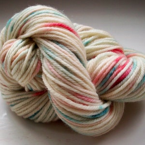 May include: A skein of off-white yarn with streaks of pink, teal, and peach. The yarn is tightly wound, showing the texture of the fibers. Ideal for knitting or crochet projects.