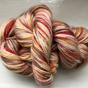 May include: A skein of yarn in a multi-colored pattern of cream, brown, red, and orange. The yarn is twisted and knotted, showing the different colors.