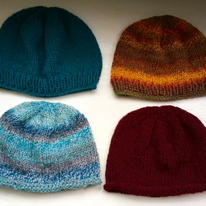 Puede incluir: Cuatro gorros de punto en diferentes colores y patrones. Los gorros son de color turquesa, marrón con rayas naranjas y amarillas, azul con rayas grises y burdeos.