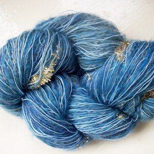 May include: A skein of blue yarn with white and gold accents. The yarn is a mix of blues, with white strands running through it. Gold metallic threads are interspersed throughout the yarn, adding a touch of sparkle. This yarn is suitable for knitting or crochet projects.