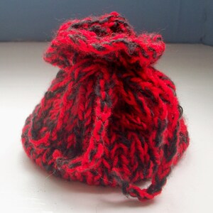 May include: A small red and black knitted drawstring bag. The bag is made with a thick yarn and has a loose, gathered top.