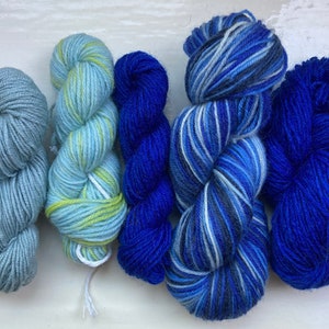 May include: Five skeins of yarn in shades of blue and green. The yarn is arranged in a row, with the lightest shade on the left and the darkest shade on the right.