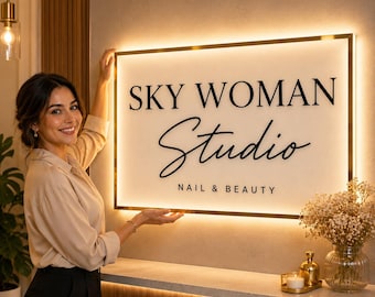 Könnte beinhalten: Ein rechteckiges Wand-Schild mit goldenem Rahmen und interner Hintergrundbeleuchtung. Das Schild zeigt den schwarzen Schriftzug SKY WOMAN STUDIO NAIL & BEAUTY in einer Kombination aus Serif- und Schreibschrift auf weißem Untergrund.