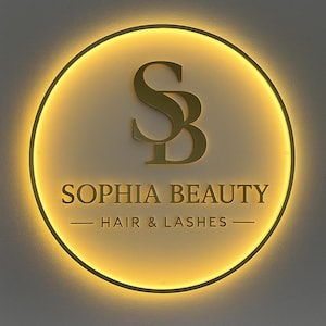 K&ouml;nnte beinhalten: Ein kreisf&ouml;rmiges Wandschild mit goldfarbenem Finish und einem leuchtend gelben Rand. In der Mitte befinden sich die Buchstaben SB, der Schriftzug SOPHIA BEAUTY und der Text HAIR & LASHES in einer passenden goldenen Schrift.