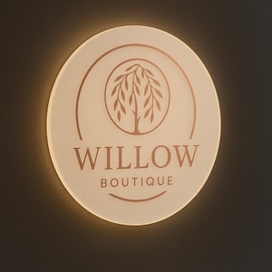 K&ouml;nnte beinhalten: Ein kreisf&ouml;rmiges, hinterleuchtetes Schild mit einer mattierten Oberfl&auml;che und einer kupferfarbenen Weidengrafik in einem Kreis. Der Text WILLOW BOUTIQUE ist in kupferfarbenen Buchstaben unter dem Baum gedruckt, mit einer geschwungenen Linie darunter.