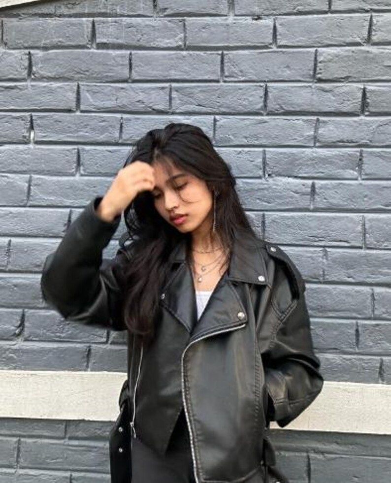 Stylish black faux leather biker jacket with asymmetric front zipper, wide lapel collar, and relaxed oversized fit inspired by vintage moto fashion and modern streetwear trends. This edgy women leather jacket delivers the perfect blend of biker style jacket, casual leatherjacket, and Y2K fashion aesthetics. Ideal for fall winter outfits, urban street style, minimalist fashion, and everyday casual wear. This trendy moto jacket pairs effortlessly with denim, boots, skirts, and layered outfits.