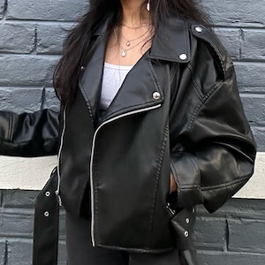Edgy black faux leather biker jacket featuring an asymmetric front zipper, wide lapel neckline, and sleek moto-inspired silhouette for a bold modern streetwear look. This trendy oversized leather jacket blends vintage moto jacket aesthetics with contemporary fashion, making it perfect for fall winter outfits, casual chic styling, Y2K streetwear, and everyday wear. Inspired by classic bikerjacket and bomber jacket trends, this women leather jacket pairs effortlessly with denim, boots.