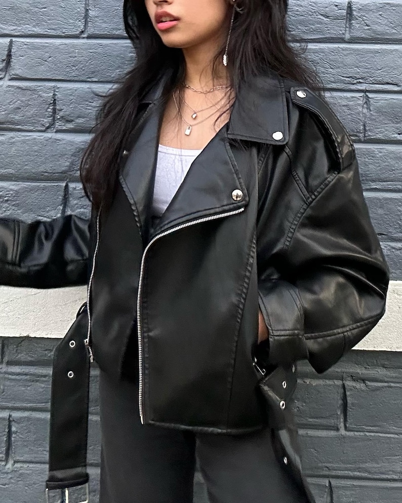 Edgy black faux leather biker jacket featuring an asymmetric front zipper, wide lapel neckline, and sleek moto-inspired silhouette for a bold modern streetwear look. This trendy oversized leather jacket blends vintage moto jacket aesthetics with contemporary fashion, making it perfect for fall winter outfits, casual chic styling, Y2K streetwear, and everyday wear. Inspired by classic bikerjacket and bomber jacket trends, this women leather jacket pairs effortlessly with denim, boots.