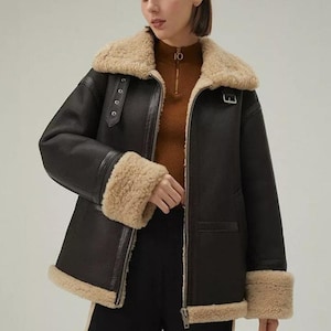 Peut inclure: Une veste en cuir noir avec un col et des poignets en peau de mouton. La veste a une fermeture éclair et une ceinture à la taille.