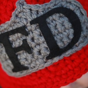 May include: Red crocheted hat with a gray crocheted patch that says "FD" in black felt letters.