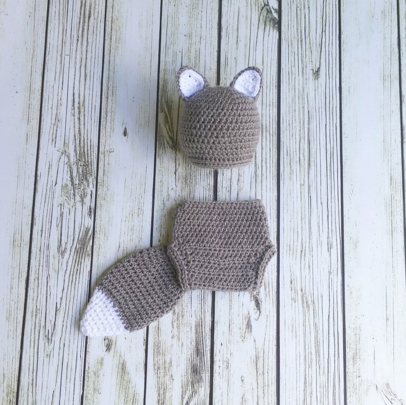 May include: A brown crocheted baby hat with white ears and a matching brown crocheted diaper cover with a tail.