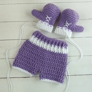 May include: A set of purple and white crocheted baby clothes, including a pair of mittens and a pair of shorts.