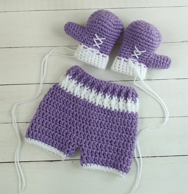 May include: A set of purple and white crocheted baby clothes, including a pair of mittens and a pair of shorts.