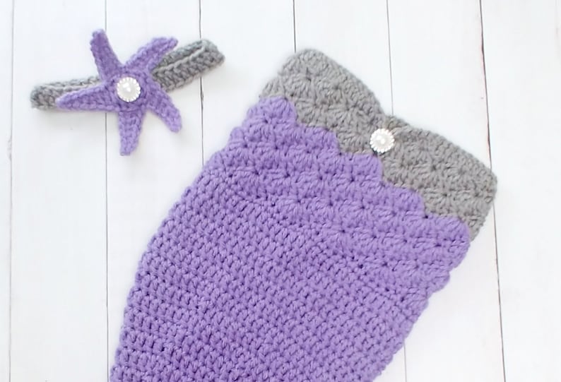 May include: A purple and gray crocheted mermaid tail costume with a matching purple starfish headband. The headband has a pearl embellishment.