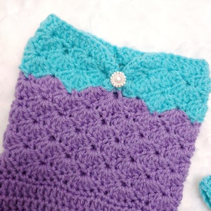 May include: A crocheted mermaid tail blanket in purple and turquoise with a pearl button.
