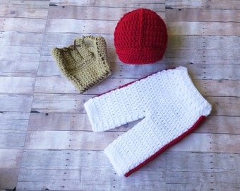 Può includere: Un completo per neonato all'uncinetto in bianco e rosso con un cappello abbinato all'uncinetto rosso e un guanto all'uncinetto marrone.