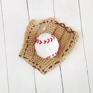 May include: A crocheted baseball mitt with a white baseball in the center. The mitt is brown and has white stitching.