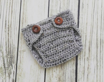 May include: A handmade, gray crocheted diaper cover with two wooden buttons. The diaper cover is designed with a simple, classic style, perfect for baby photoshoots or as a unique baby shower gift. The neutral color makes it suitable for any baby.