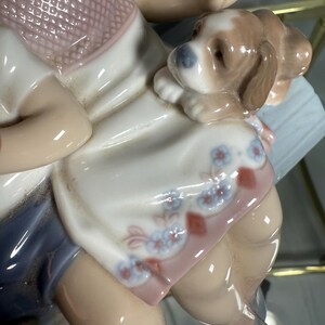 May include: A porcelain figurine of a child with a puppy. The child is wearing a pink top and blue shorts. The puppy is brown and white. The figurine has a glossy finish and is highly detailed.