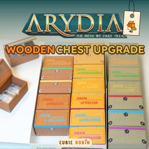 May include: Wooden chest upgrade for the board game Arydia. The image shows several small, rectangular boxes with labels like "Path of Inspiration" and "Path of Valor." The boxes are various colors, including brown, yellow, and green. The game's logo is at the top.